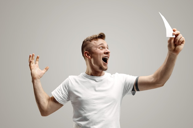 Young caucasian man with a surprised happy expression won a bet on gray studio background. Human facial emotions and betting concept