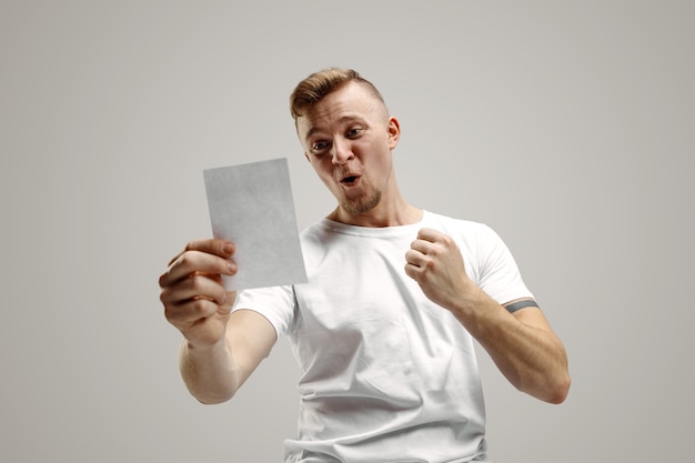 Young caucasian man with a surprised happy expression won a bet on gray studio background. Human facial emotions and betting concept