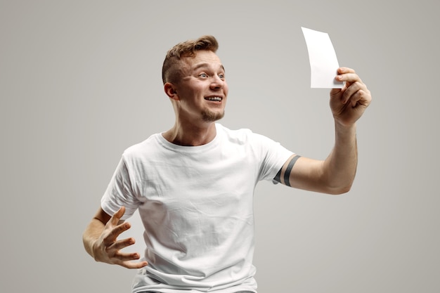 Free photo young caucasian man with a surprised happy expression won a bet on gray studio background. human facial emotions and betting concept