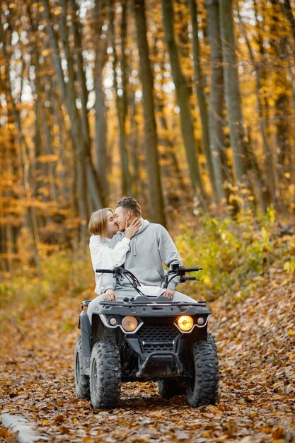 秋の森でATVクワッドバイクに乗る若い白人の男性と女性灰色のスポーティーな衣装を着てカップルにキスする素敵なカップル