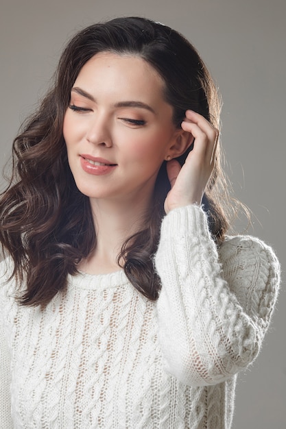 Young caucasian model with long dark hair poses for the camera with hand near her face