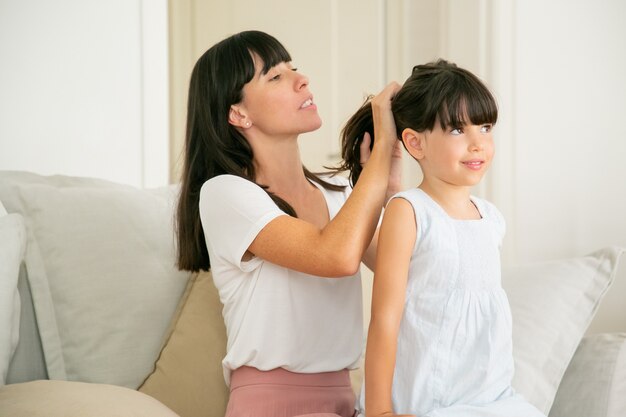 Young Caucasian mother holding hairs of her daughter