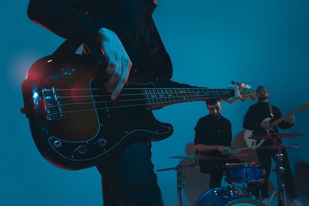 Young caucasian musicians, band performing in neon light on blue studio