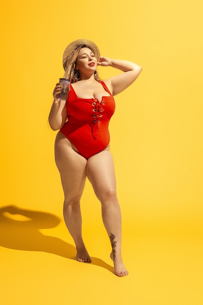 Young caucasian plus size female model's preparing for beach resort on yellow