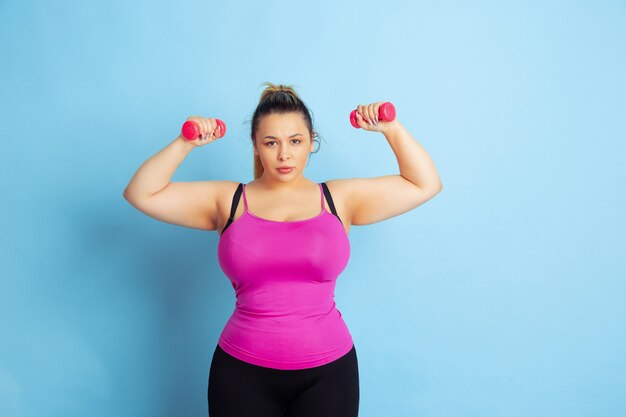 Free photo young caucasian plus size female model's training on blue background