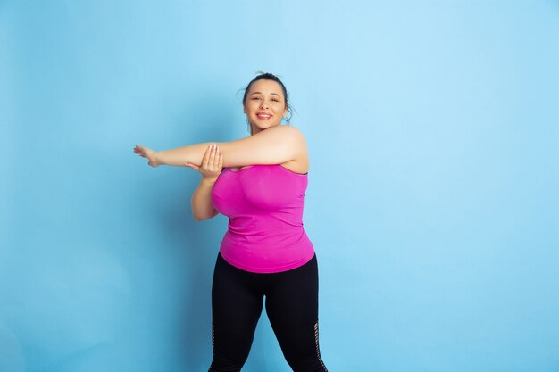 Young caucasian plus size female model's training on blue space