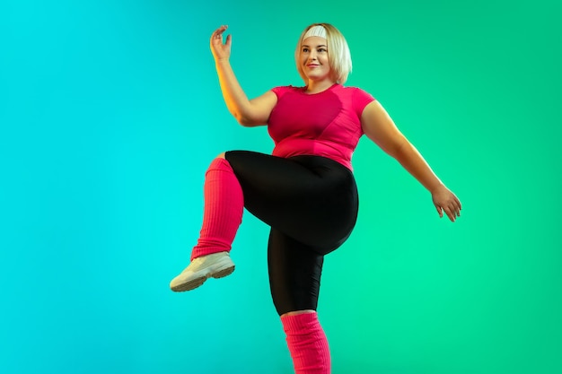 Free photo young caucasian plus size female model's training on gradient green background in neon light.