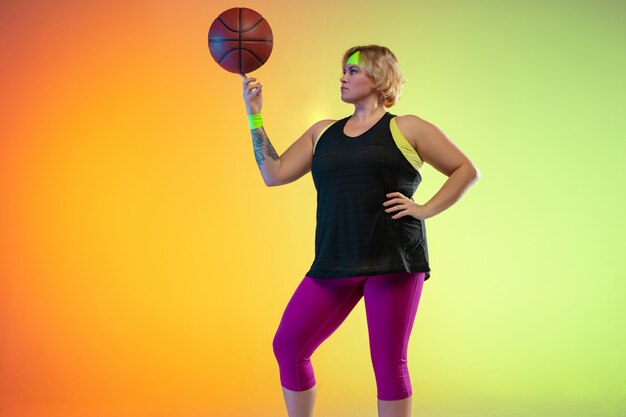 Young caucasian plus size female model's training on gradient orange wall in neon light.