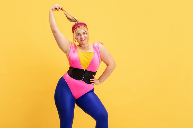 Young caucasian plus size female model training on yellow