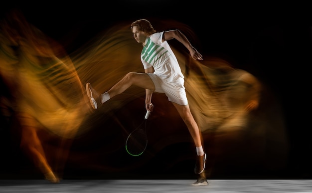 Молодой кавказский профессиональный спортсмен играет в теннис на черной стене в смешанном свете