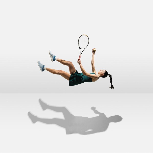Молодая кавказская профессиональная спортсменка парит в воздухе во время игры в теннис на белом фоне