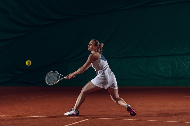 Молодая кавказская профессиональная спортсменка, играющая в теннис на стене спортивной площадки.