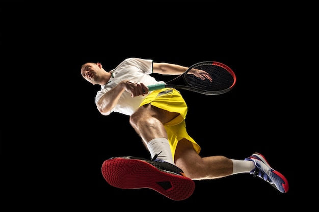 Free photo young caucasian tennis player in action, motion isolated on black wall, look from the bottom. concept of sport, movement, energy and dynamic, healthy lifestyle. training, practicing.