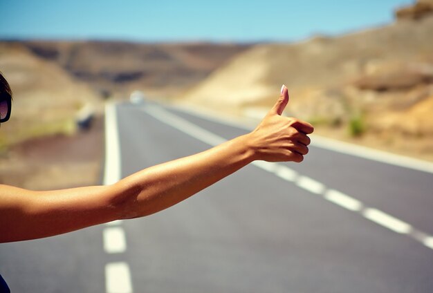 Young caucasian tourist hitchhiking along a road in sunset