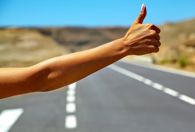 Young caucasian tourist hitchhiking along a road in sunset