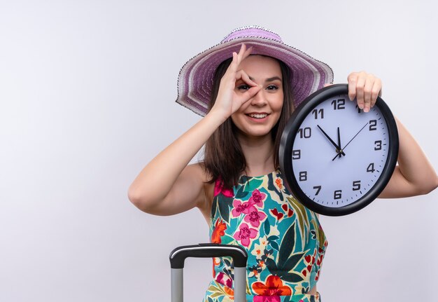 Young caucasian traveler girl wearing hat holding clock on isolated white background