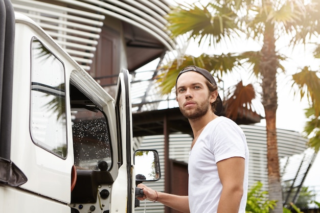 Young Caucasian traveler in snapback getting in his white off-road vehicle, ready to drive to safari race