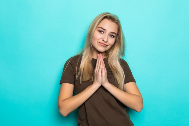 Young caucasian woman holding hands in pray isolated on blue wall