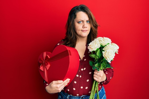 Free photo young caucasian woman holding valentine gift and flowers skeptic and nervous frowning upset because of problem negative person