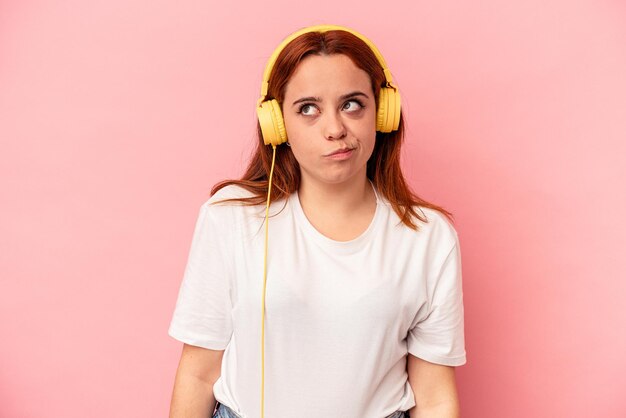 ピンク​の​背景​に​分離された​音楽​を​聞いている​若い​白人​女性​は​混乱し​、​疑わしく​、​不安​を​感じています​。