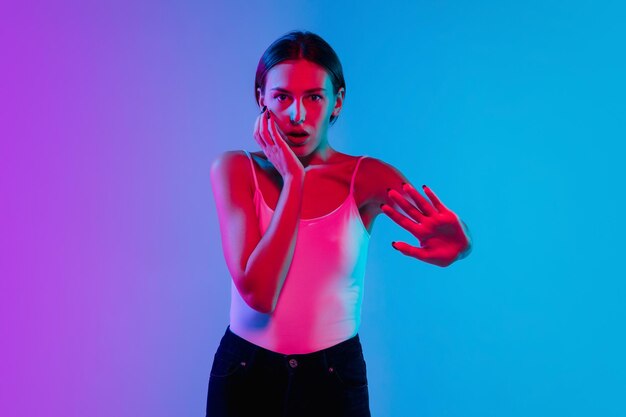 Young caucasian woman's portrait on gradient blue-purple studio in neon light