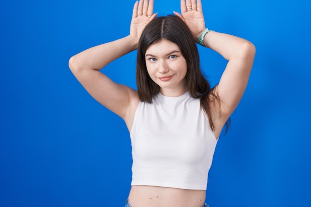 Young caucasian woman standing over blue background doing bunny ears gesture with hands palms looking cynical and skeptical easter rabbit concept