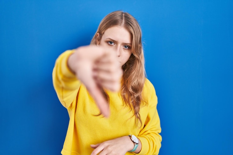 Free Photo young caucasian woman standing over blue background looking unhappy and angry showing rejection and negative with thumbs down gesture bad expression