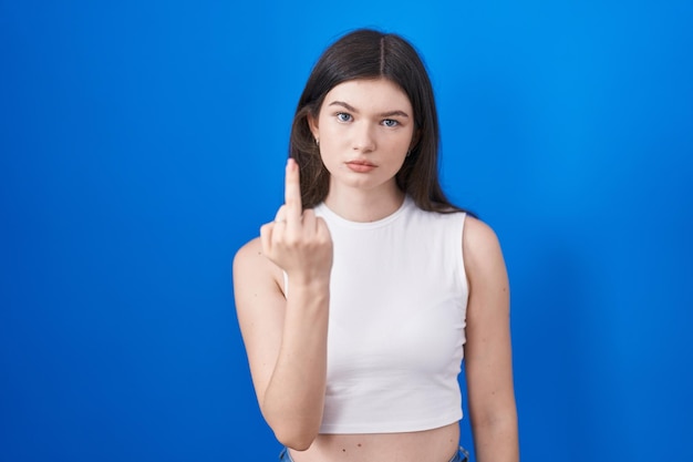 Free photo young caucasian woman standing over blue background showing middle finger impolite and rude fuck off expression