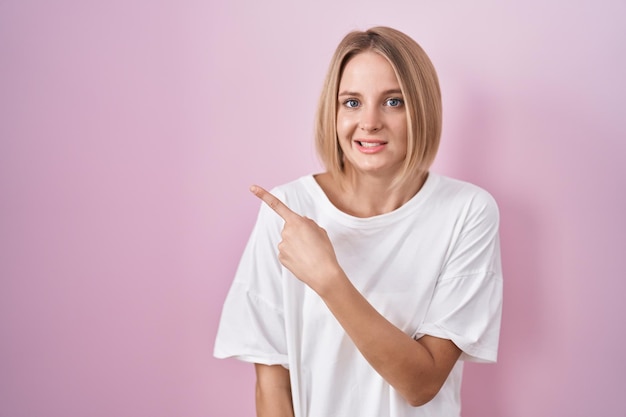 Free photo young caucasian woman standing over pink background pointing aside worried and nervous with forefinger concerned and surprised expression