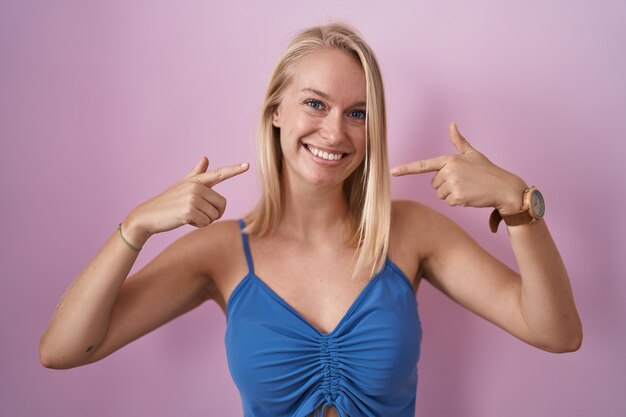 Young caucasian woman standing over pink background smiling cheerful showing and pointing with fingers teeth and mouth. dental health concept.