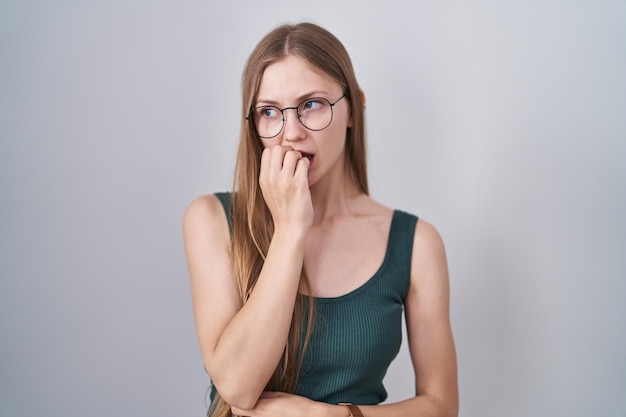 Free photo young caucasian woman standing over white background looking stressed and nervous with hands on mouth biting nails anxiety problem