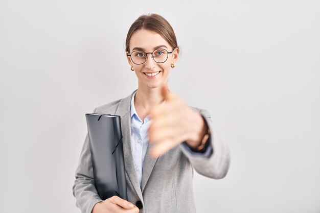 Young caucasian woman wearing business clothes and glasses smiling friendly offering handshake as greeting and welcoming. successful business.