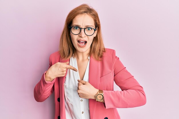 Young caucasian woman wearing business style and glasses in hurry pointing to watch time impatience upset and angry for deadline delay