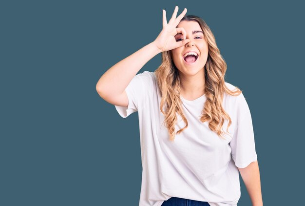 Young caucasian woman wearing casual clothes doing ok gesture with hand smiling eye looking through fingers with happy face