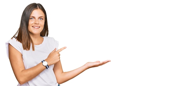 Free photo young caucasian woman wearing casual white tshirt amazed and smiling to the camera while presenting with hand and pointing with finger.