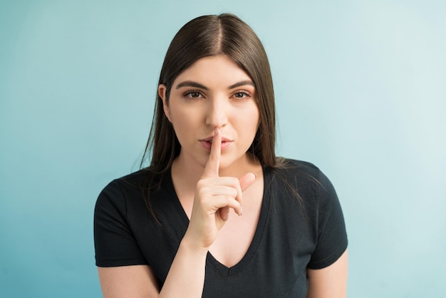 Young Caucasian woman with finger on lips while making eye contact against plain background