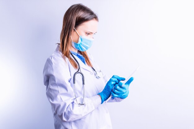 タブレット​ポイント​の​概念​医学​と​技術​の​接続性​に関する​医療​レポート​を​見て​マスク​ガウン​と​聴診器​を​持つ​若い​白人​女性
