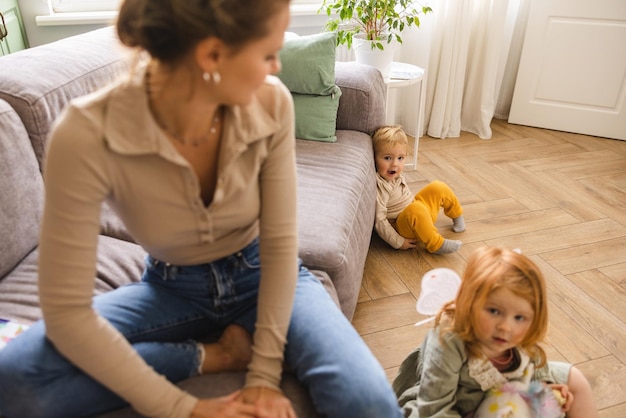 Young caucasian woman with two redhaired children girl and boy spend time in light living room Family concept