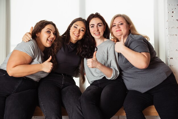 Young caucasian women in casual clothes having fun together. Friends sitting near by window and laughting, spending time together. Bodypositive, nutrition, feminism, loving themself, beauty concept.