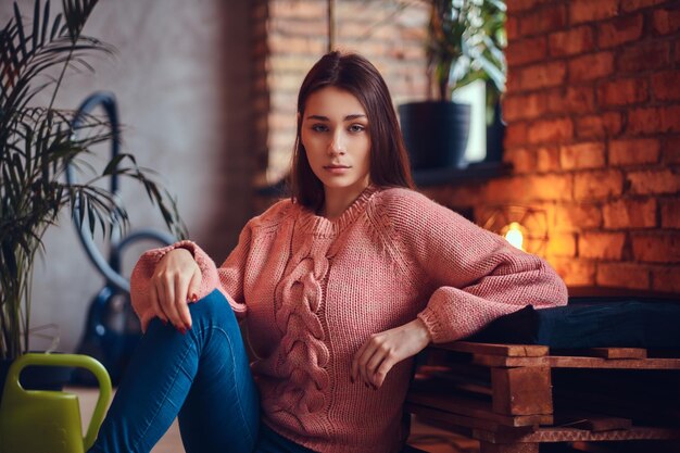 Young charming brunette in stylish clothes sits on a floor. Relaxing after cleaning in a room with loft interior.