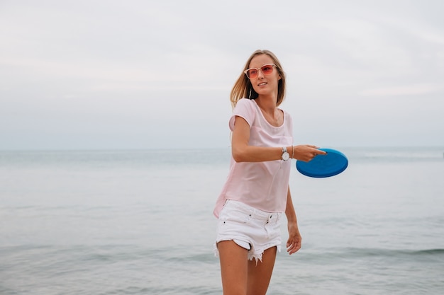 Young charming woman playing frisbee near the sea, holding frisbee disk. 