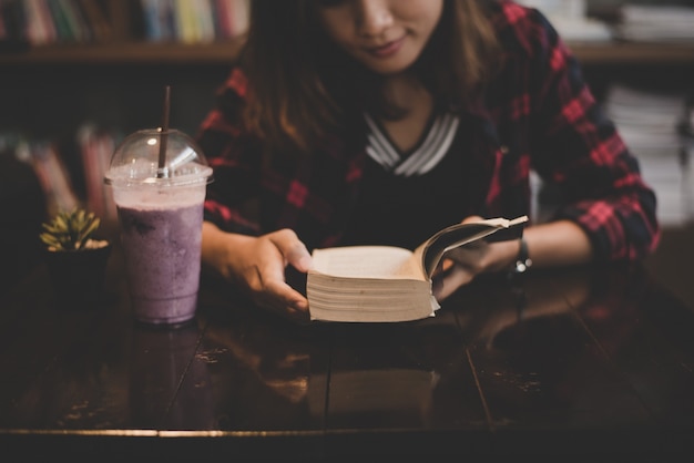 Young charming woman with milkshake and reading book sitting indoor in cafe. Casual portrait of teenage girl.