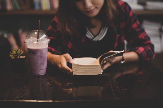 Молодая очаровательная женщина с молочный коктейль и чтение книги, сидя в помещении в кафе. Случайный портрет девочки-подростка.