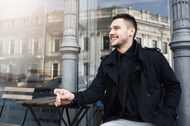 Young cheeful man smoking cigarette, smiling cheerfully, looking away.