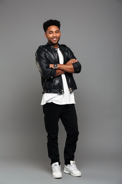 young cheerful african boy in leather jacket standing with crossed hands, looking