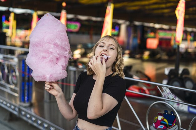 遊園地で綿菓子を食べる若い陽気な白人女性