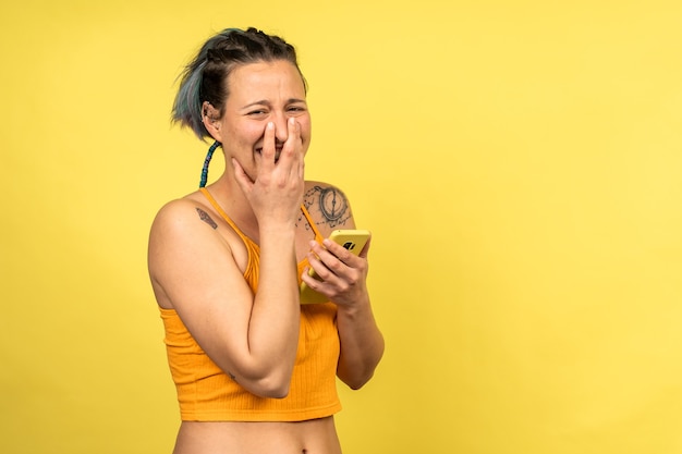 Young cheerful Caucasian female with nice tattoos laughing while going through her phone