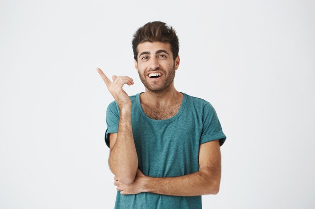 Young cheerful caucasian unshaven guy in casual t-shirt, looking really happy after remembering about day off work tomorrow.