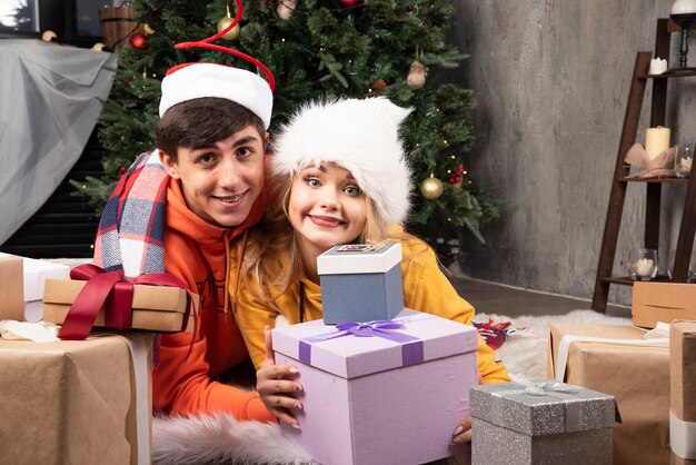 Young cheerful couple in love posing with gifts for Christmas in living room.
