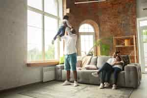 Free photo young and cheerful family during quarantine, insulation spending time together at home.